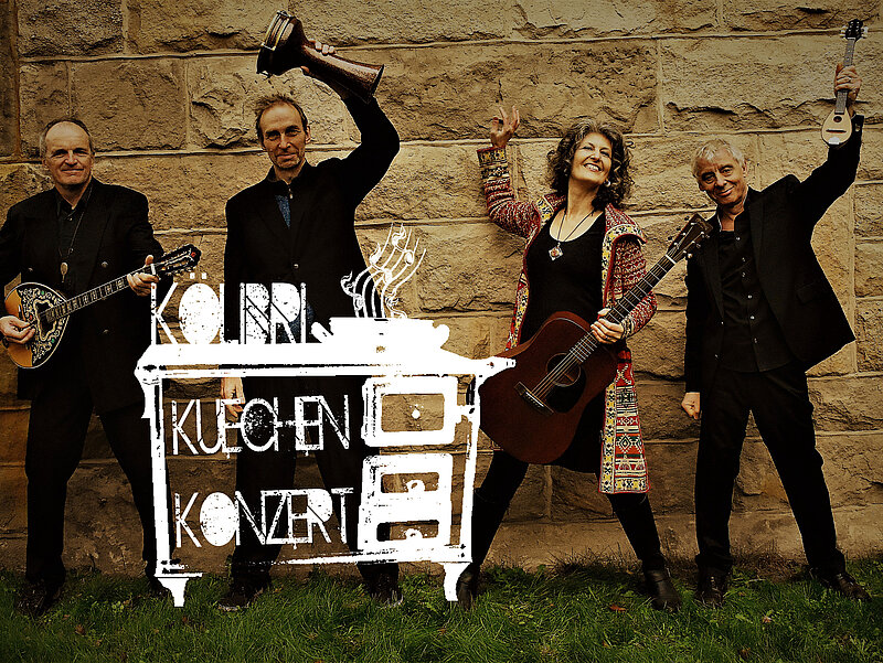Die vierköpfige Band steht lächelnd vor einer Natursteinmauer und präsentiert ihre Instrumente. Davor in weiß das Logo vom Küchenkonzert, ein alter Herd.