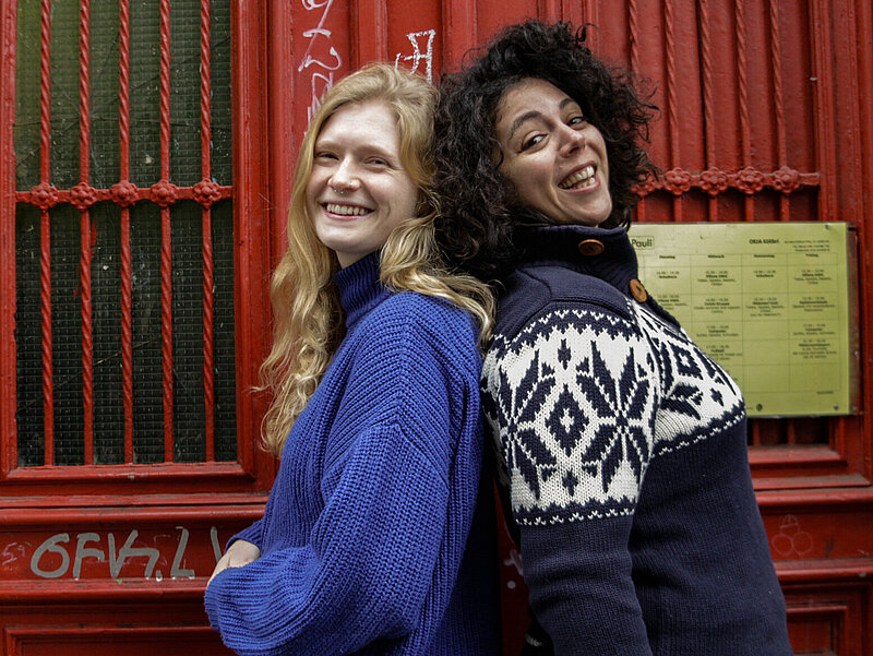 Carmen und Nele stehen Rücken an Rücken vor der Eingangstür vom Kinderclub