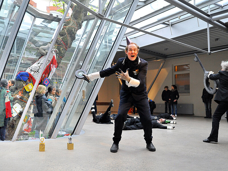 Schwarzgekleidete Schauspielende in einer modernen Passage.