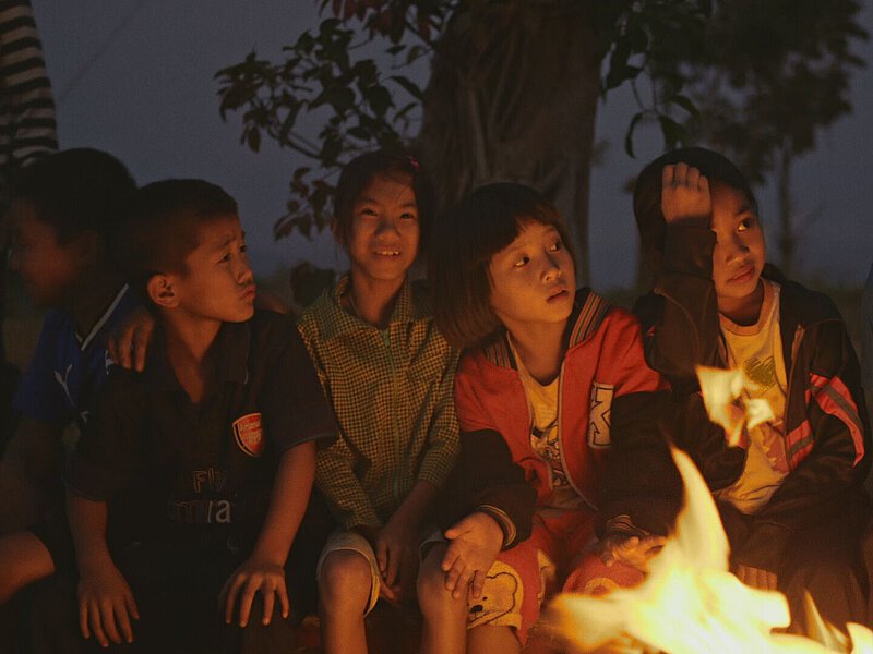 Mehrere Kinder sitzen während der Abenddämmerung draußen vor einem Feuer