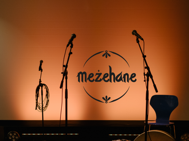 Leere Bühne und Mikrophonständer im Gegenlicht. Schriftzug Mezehane.