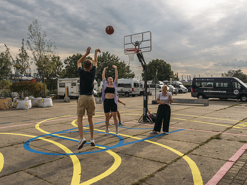 4 Personen spielen auf einem improvisiertes Basketballfeld auf der Freifläche der Hafenkante.