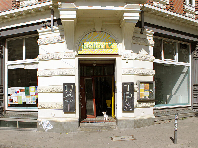 Der Eingang des Kölibris. Ein kleiner Hund sitz vor der Tür. Die Tafeln sind mit den Buchstaben UTOPIA beschriftet.