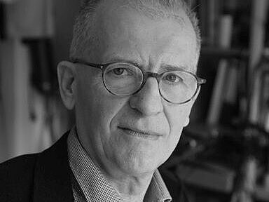 Schwarz-weiß Portrait des Autors. Ein ernst blickender Mann mit schmalem Gesicht und Brille.