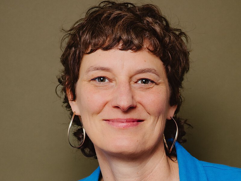 Portrait von Nele Palmtag. Sie hat kurze braune gelockte Haare und lächelt in die Kamera.