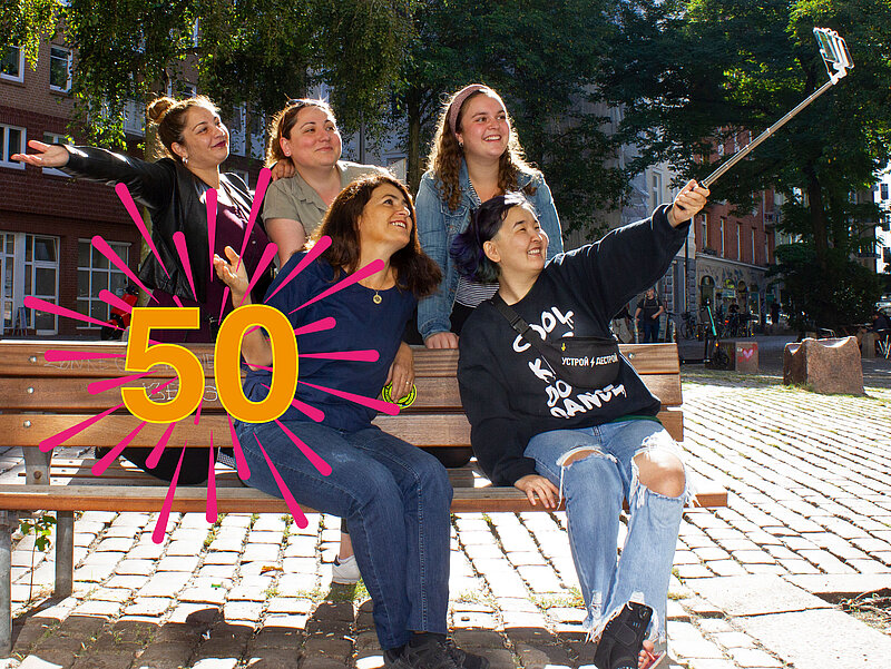5 Frauen aus der Filmcrew sitzen auf der Bank und machen ein Selfie. Das Logo von 50 Jahre GWA St. Pauli.