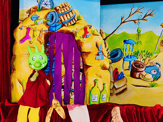 Eine Olchi-Puppe sitzt am Bühnenrand vor einem Müllberg